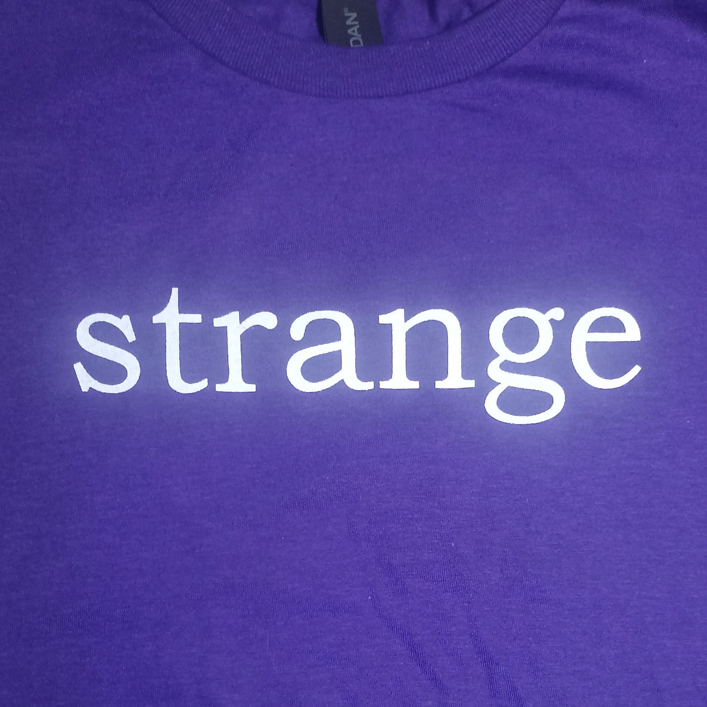 Strange Angel Exclusive Purple t-shirt with the word 'strange' printed in white on a plain background