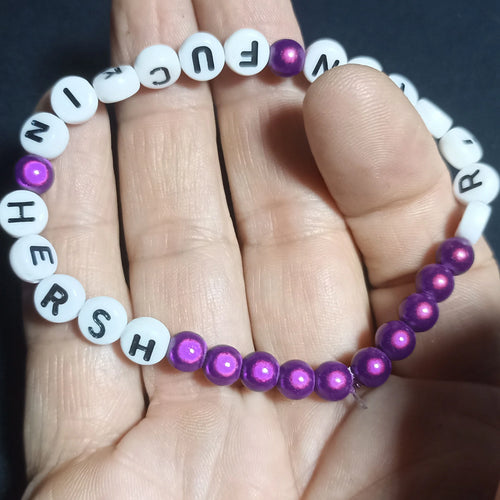 Bracelet with letter beads spelling out 'KRISTIN FN HERSH' on a hand against a dark background, Purple