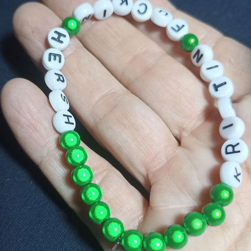 Bracelet with letter beads spelling out 'KRISTIN FN HERSH' on a hand against a dark background, Green