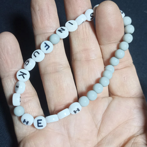 Bracelet with letter beads spelling out 'KRISTIN FN HERSH' on a hand against a dark background, Grey