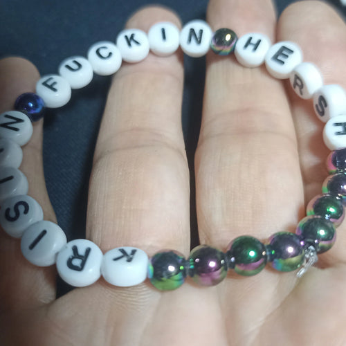 Bracelet with letter beads spelling out 'KRISTIN FN HERSH' on a hand against a dark background, Rainbow