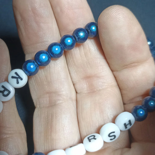 Blue beaded Kristin Hersh bracelet with white letter beads on a hand against a dark background, Clear Dark Blue