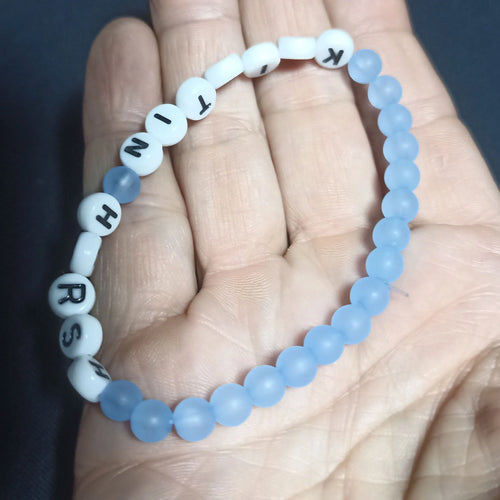 Blue beaded Kristin Hersh bracelet with white letter beads on a hand against a dark background, Crystal
 pale Blue