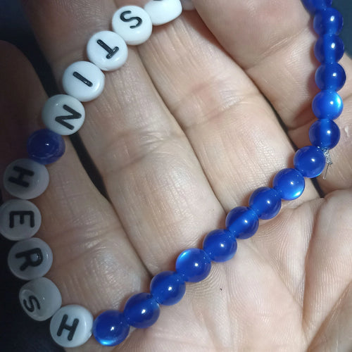 Blue beaded Kristin Hersh bracelet with white letter beads on a hand against a dark background, clear Mid Blue