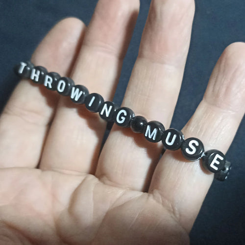 Bracelet with letter beads spelling 'THROWING MUSES 2025' on a dark background from ElRat Designs