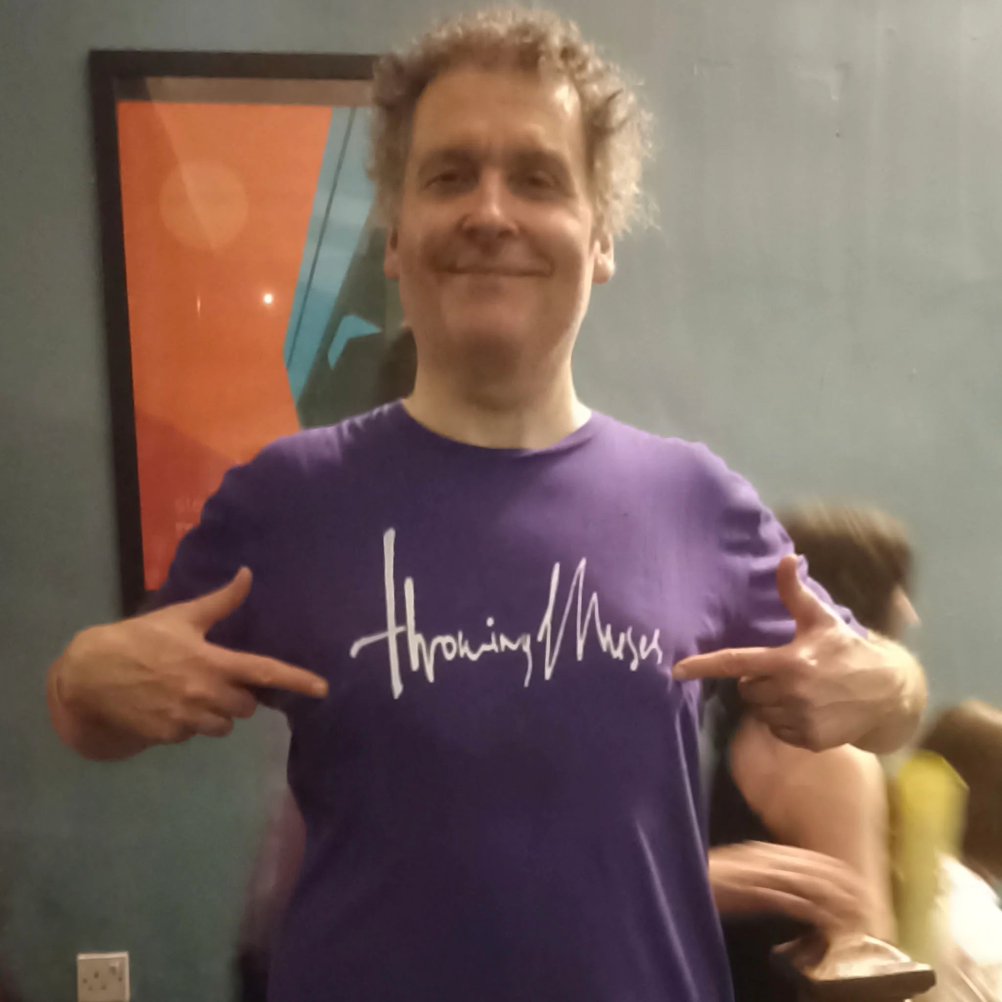 Massive ElRat Designs supporter,  and Kristin Hersh listener, Mr PG sporting one of his many ElRat Designs shirts in the wild, Her the Throwing Muses 1986 logo in Purple and White at the TM gig in Hebden Bridge on the 25th August 2025